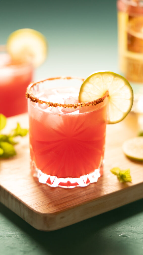 Bright pink watermelon margarita on the rocks, with a lime wheel garnish.