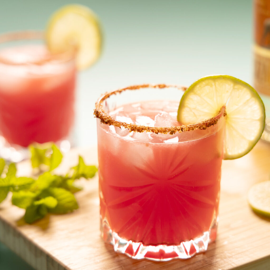 Bright pink watermelon margarita on the rocks, with a lime wheel garnish.