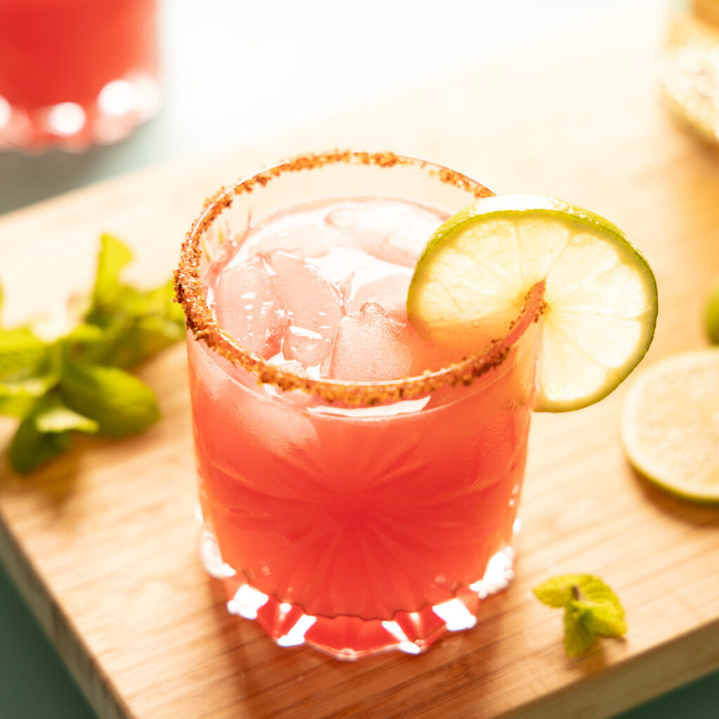 Bright pink watermelon margarita on the rocks, with a lime wheel garnish.