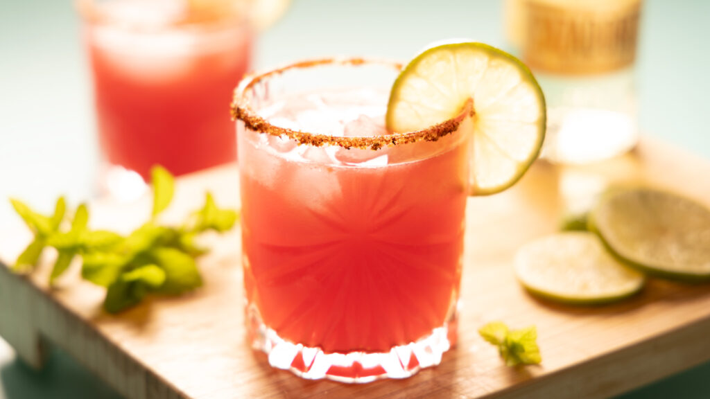 Bright pink watermelon margarita on the rocks, with a lime wheel garnish.