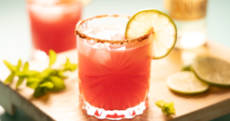 Bright pink watermelon margarita on the rocks, with a lime wheel garnish.