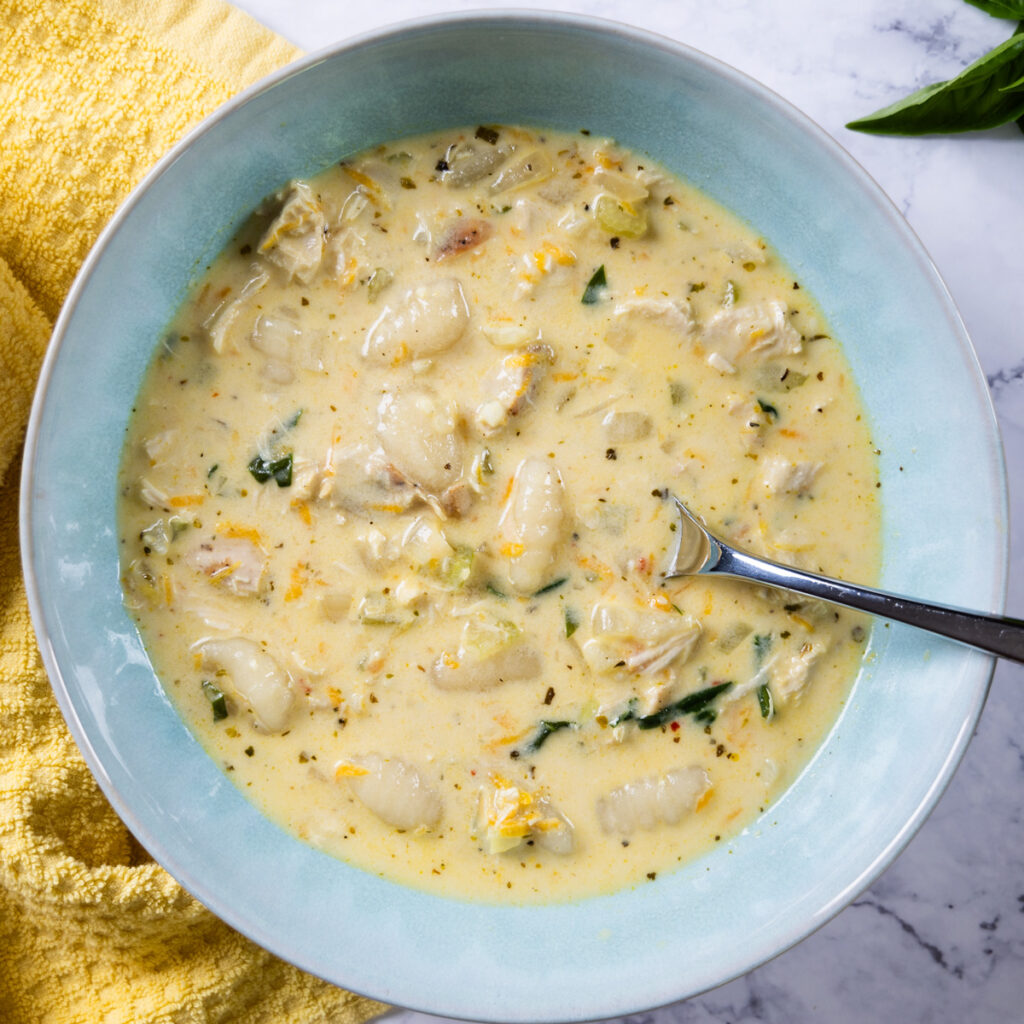 A bowl of creamy chicken and gnocchi soup in a bowl, with a yellow towel.