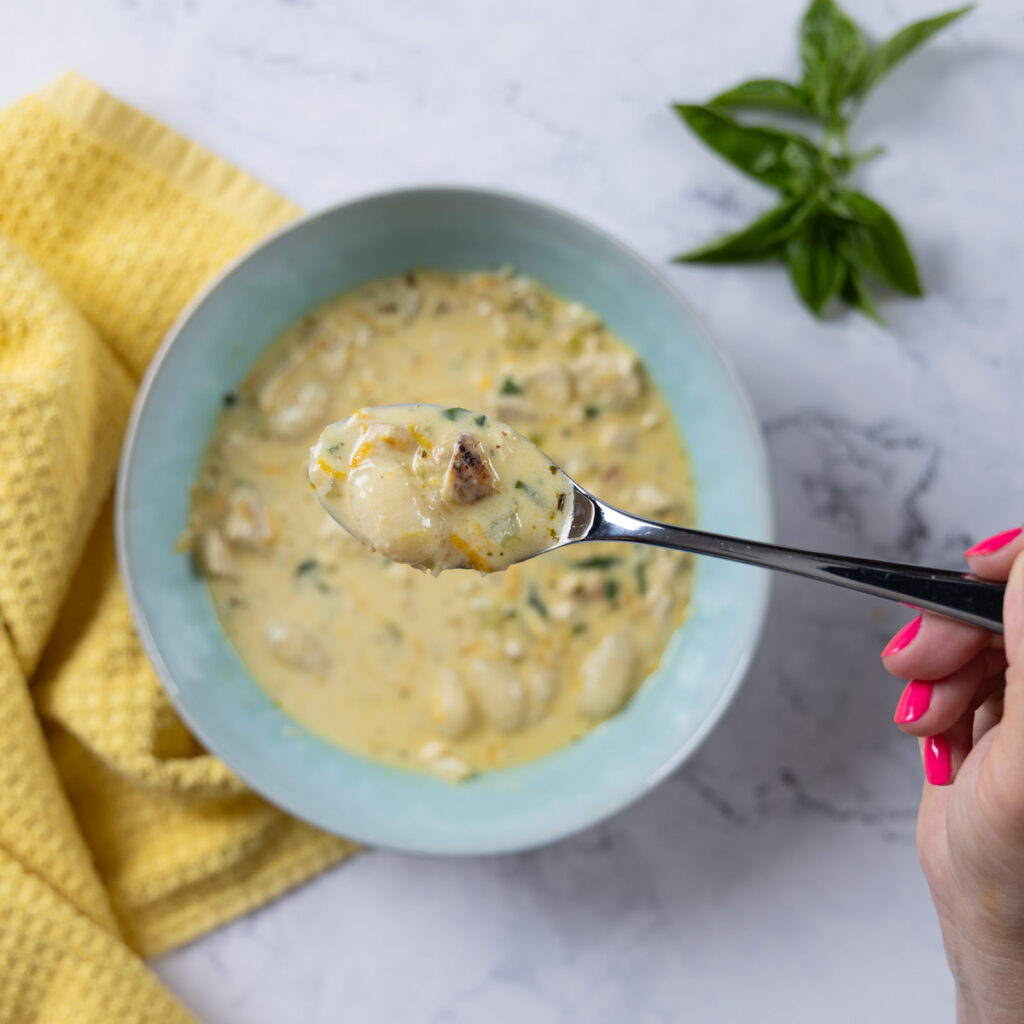 A bowl of creamy chicken and gnocchi soup in a bowl, with a yellow towel.
