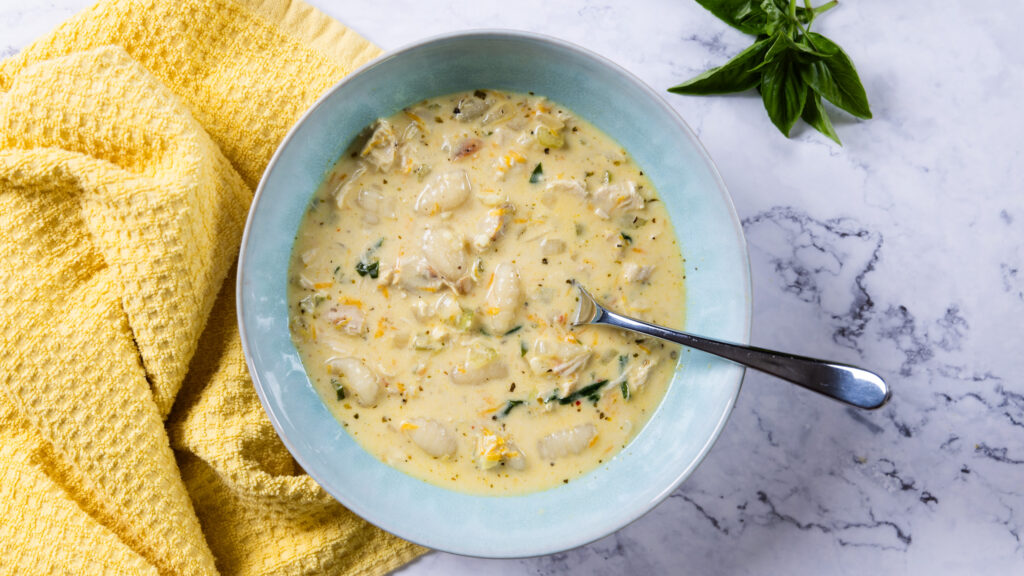 A bowl of creamy chicken and gnocchi soup in a bowl, with a yellow towel.