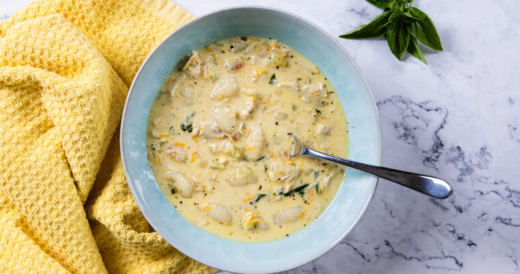 A bowl of creamy chicken and gnocchi soup in a bowl, with a yellow towel.