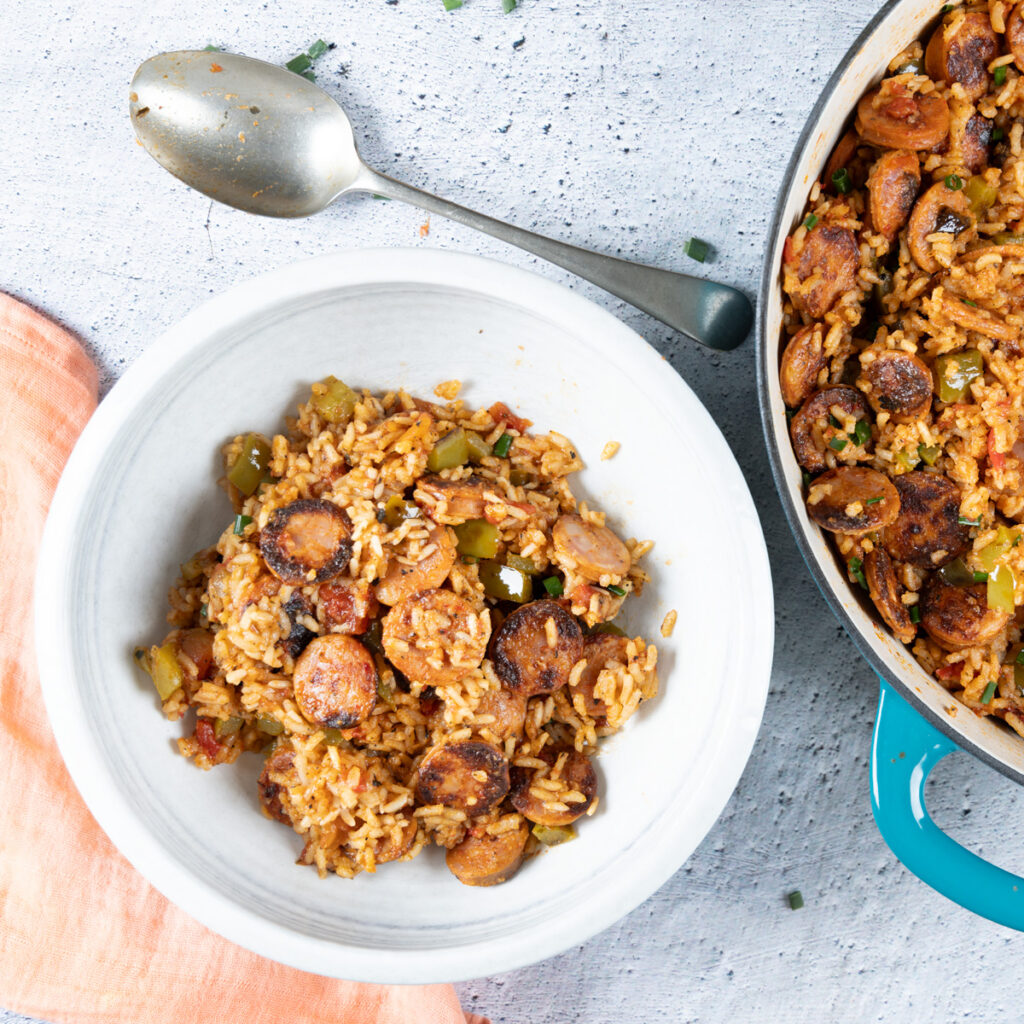 A bowl holds a chorizo sausage and rice dish. To the side, A large skillet holds a chorizo sausage