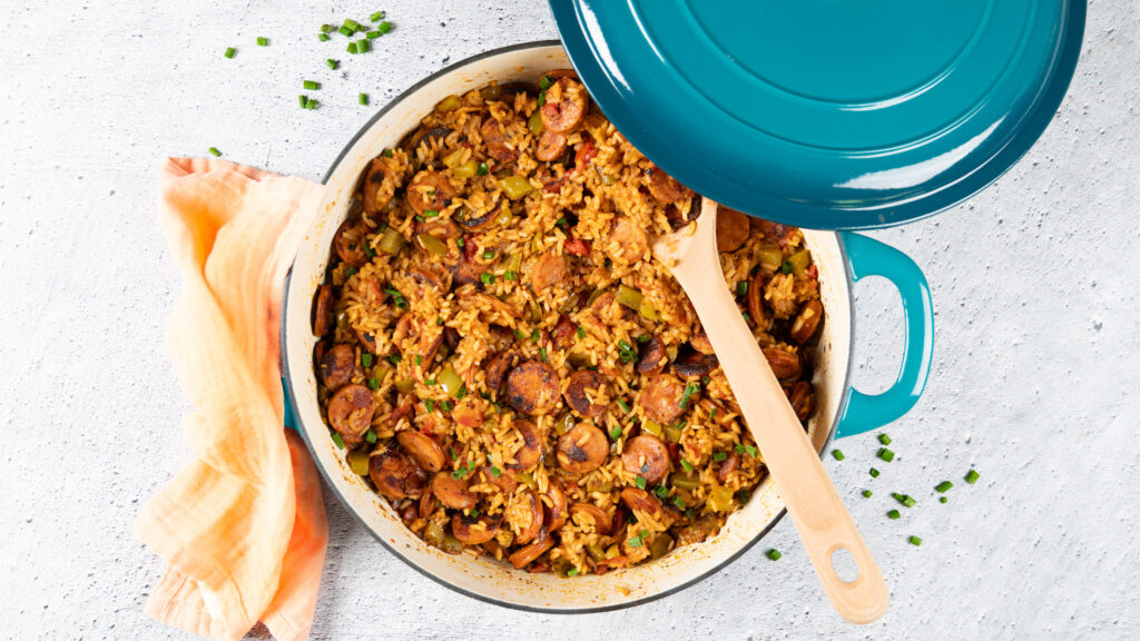 A large skillet holds a chorizo sausage and rice dish. A large wooden spoon is in the skillet.