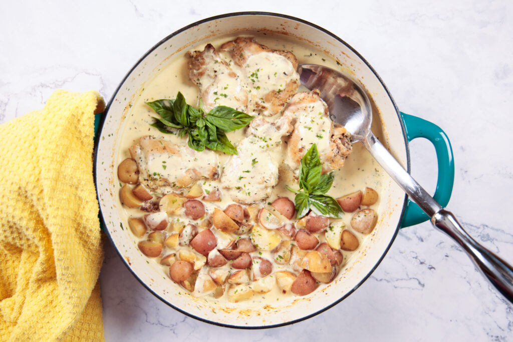 A large skillet with chicken and baby potatoes, in a creamy Dijon mustard sauce.