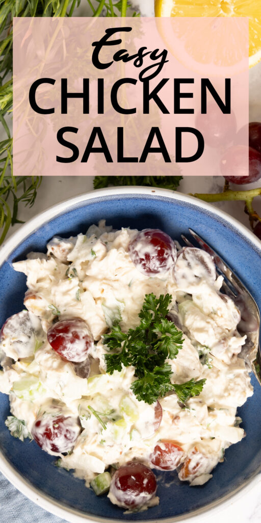 An image for Pinterest. A small bowl contains chicken salad. In the salad is creamy dressing, red grapes, chunks of chicken, bits of celery, onion, and herbs. Next to the bowl are pecans, bunches of herbs, a cut lemon, and red grapes. A blue napkin is next the bowl. Text on the image reads "Easy Chicken Salad"