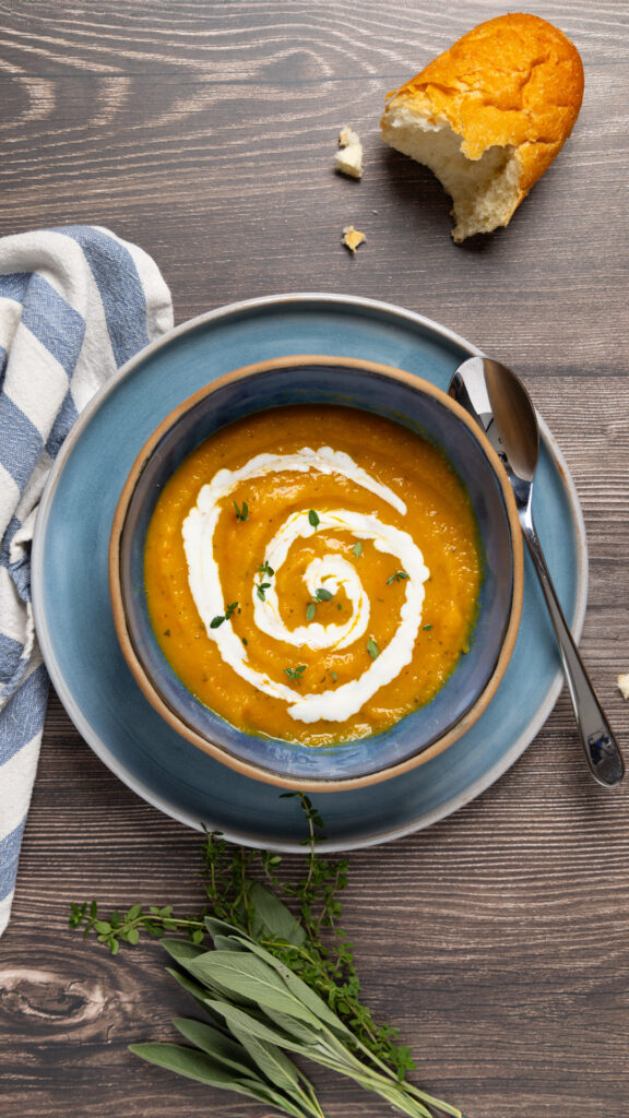 Butternut squash soup with a swirl of yogurt in a bowl. A blue and white towel is next to the bowl.