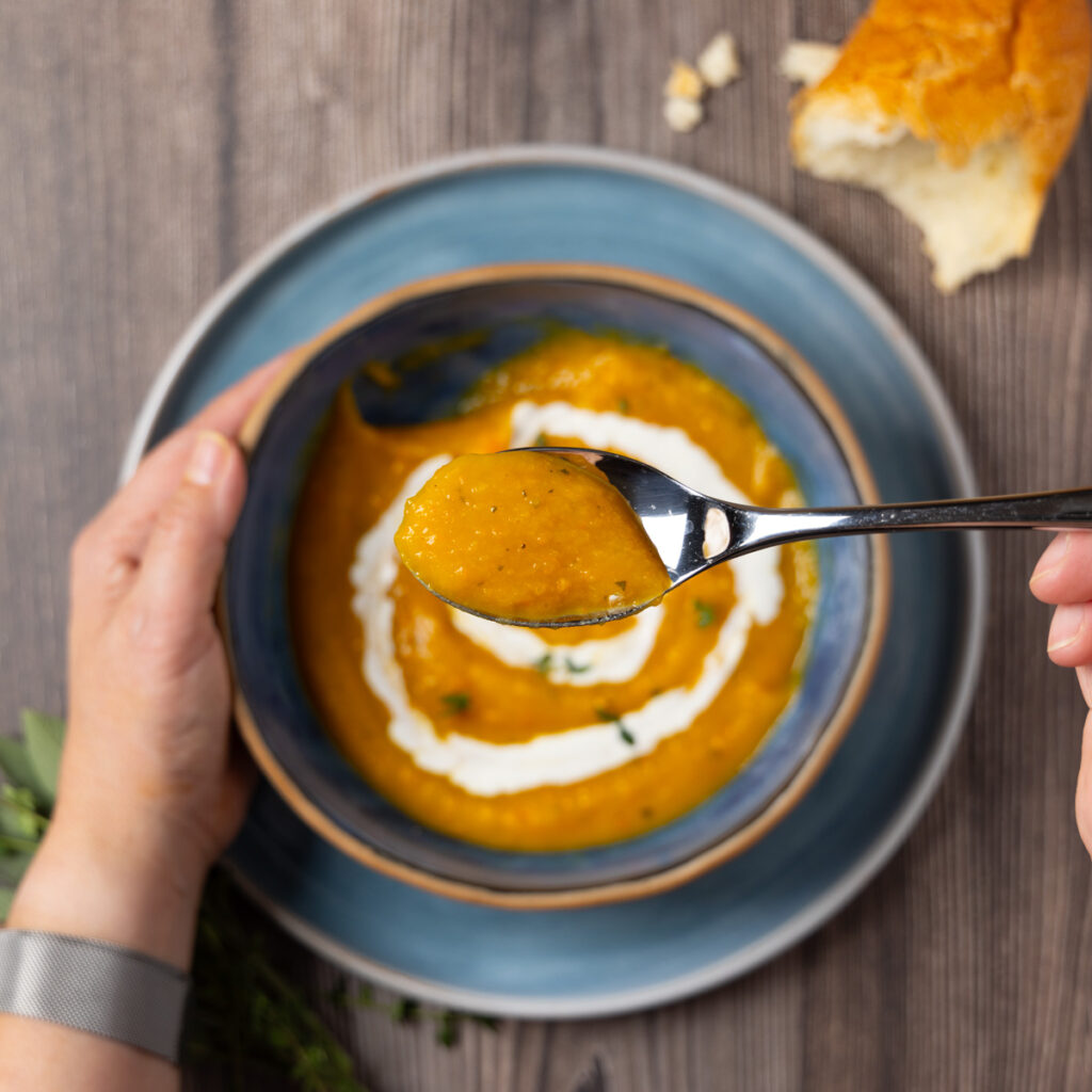 Butternut squash soup with a swirl of yogurt in a bowl. A spoonful of soup is held up to the camera.