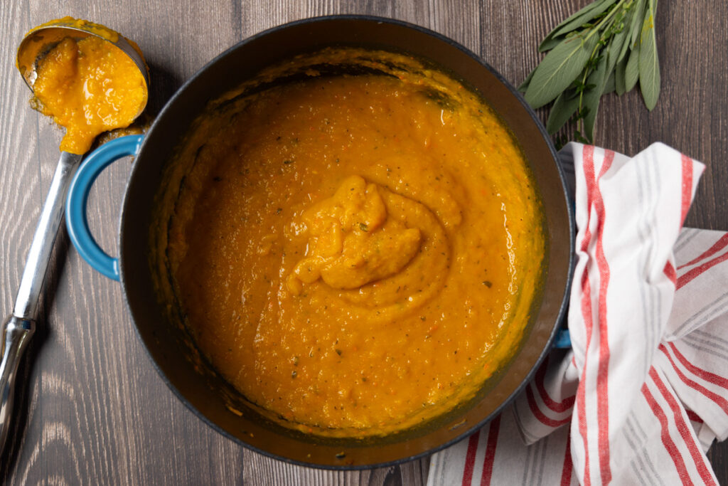 Butternut squash soup with a swirl of yogurt in a pot. A red and white towel is next to the pot.