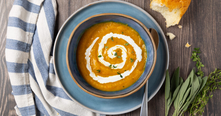 Butternut squash soup with a swirl of yogurt in a bowl. A blue and white towel is next to the bowl.