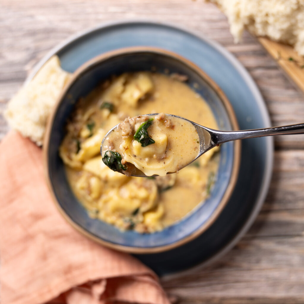 A bowl of creamy sausage, spinach, and tortellini soup.