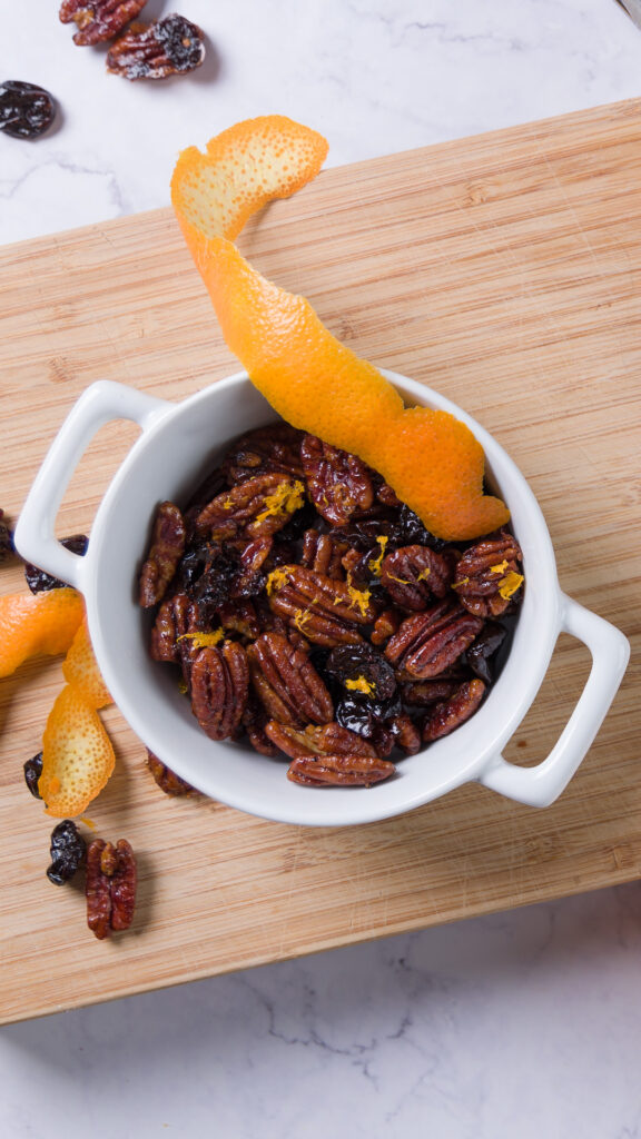 A bowl of sweet and spicy glazed pecans with bits of dried cherry and orange zest.