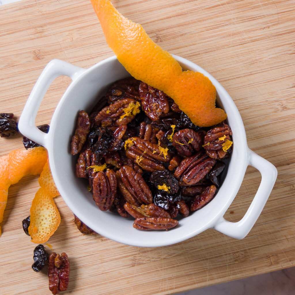 A bowl of sweet and spicy glazed pecans with bits of dried cherry and orange zest.