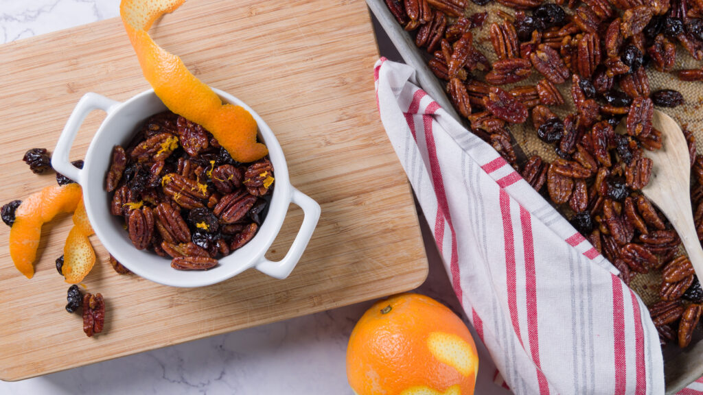 A bowl of sweet and spicy glazed pecans with bits of dried cherry and orange zest.