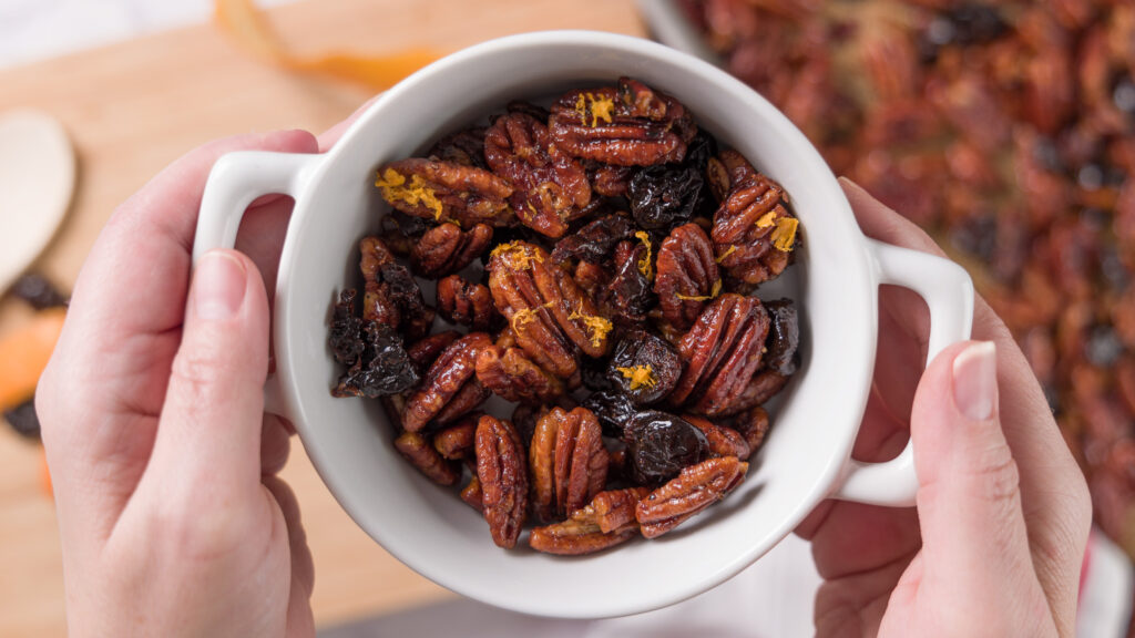 A bowl of sweet and spicy glazed pecans with bits of dried cherry and orange zest.