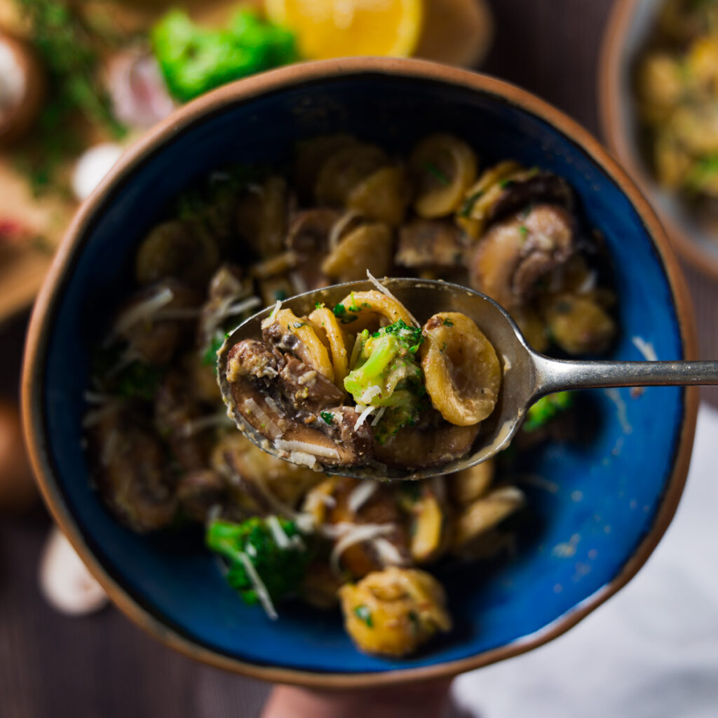 A bowl contains a pasta dish with mushrooms, broccoli, and a creamy sauce.