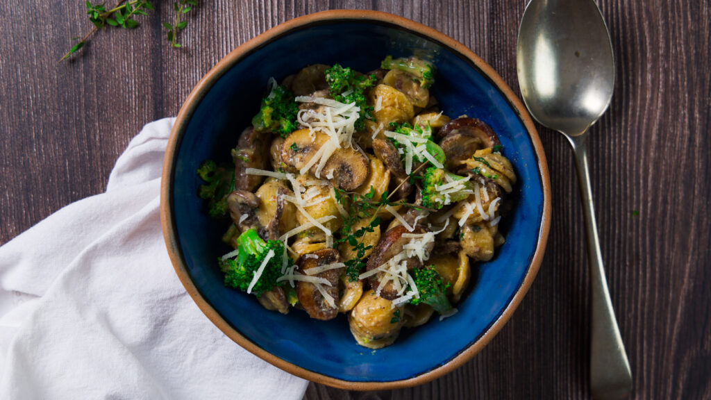 A bowl contains a pasta dish with mushrooms, broccoli, and a creamy sauce.