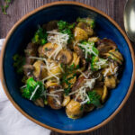 A bowl contains a pasta dish with mushrooms, broccoli, and a creamy sauce.