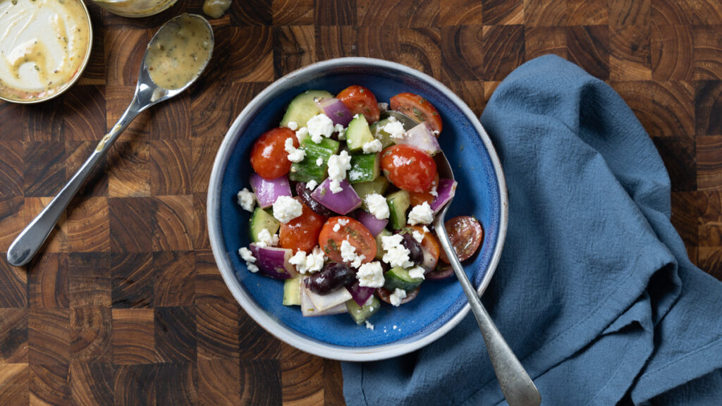 Greek salad containing tomatoes, cucumbers, olives, red onion, and feta cheese.