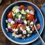 Greek salad containing tomatoes, cucumbers, olives, red onion, and feta cheese.