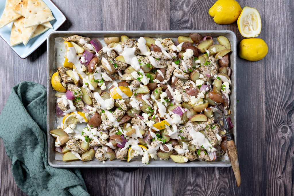 A sheet pan contains greek chicken and potatoes