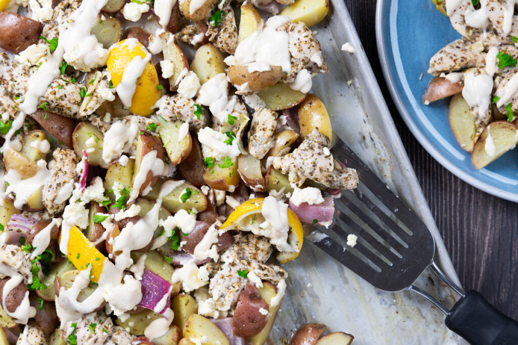 A sheet pan contains greek chicken and potatoes