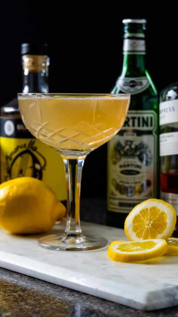 A limoncello cocktail in a crystal glass, bottles of liquor nearby and lemons