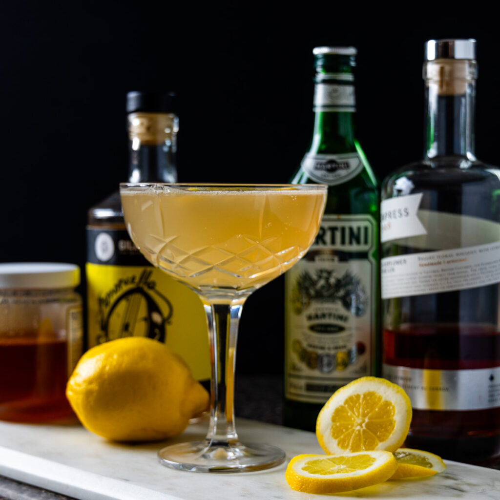 A limoncello cocktail in a crystal glass, bottles of liquor and lemons nearby