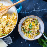 Photo of summer squash pasta in a bowl with a spoon, next to a skillet with more pasta.