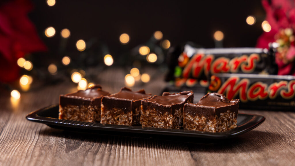 A plate of cut up rice krispie treats, with Mars Bar candy bars in the background.