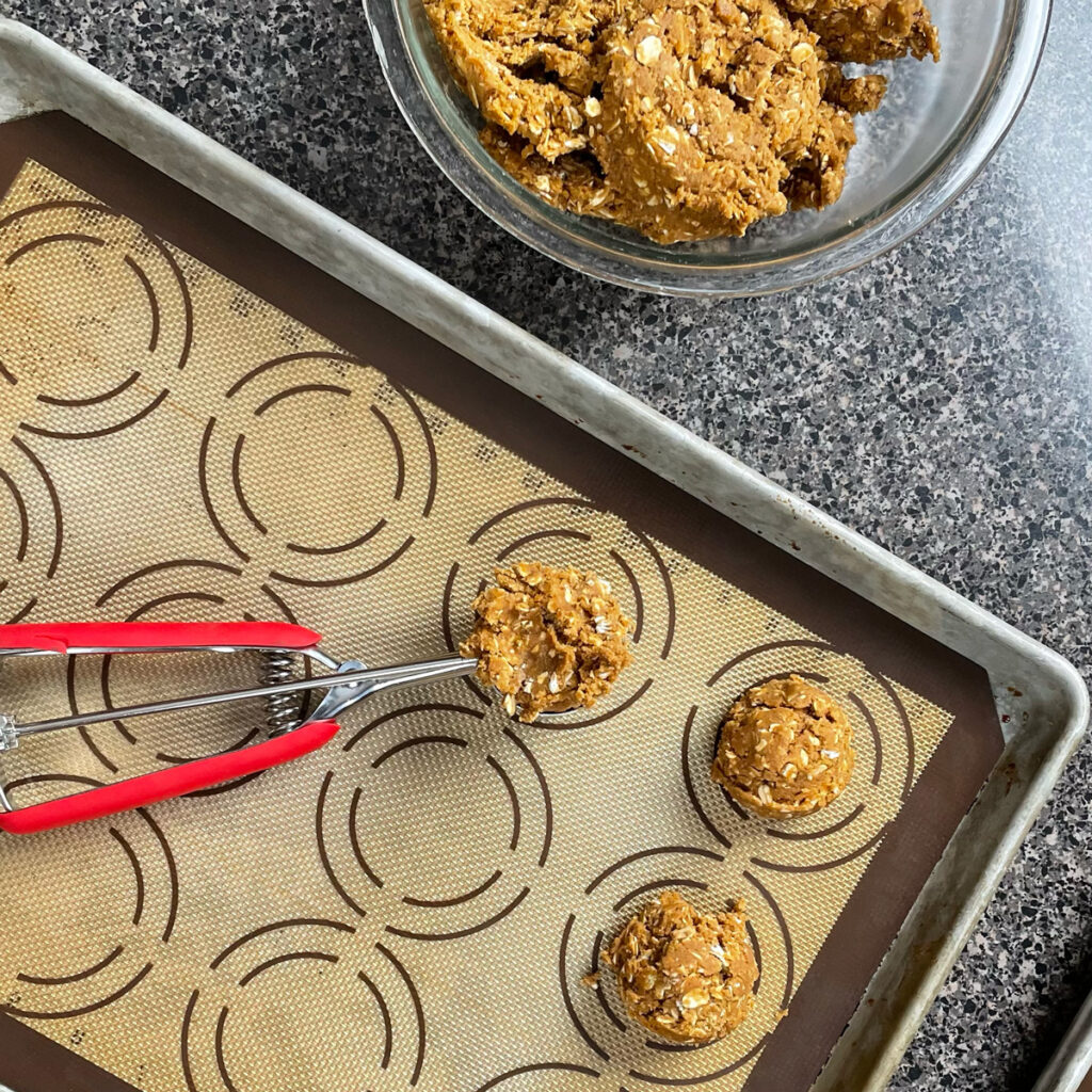 Gingerbread oatmeal cookie dough behing scooped onto a cookie sheet.