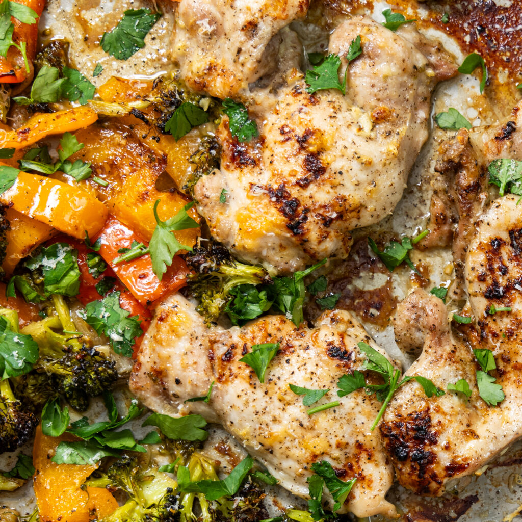 A close up view of balsamic chicken on a sheet pan, with bell peppers and broccoli.