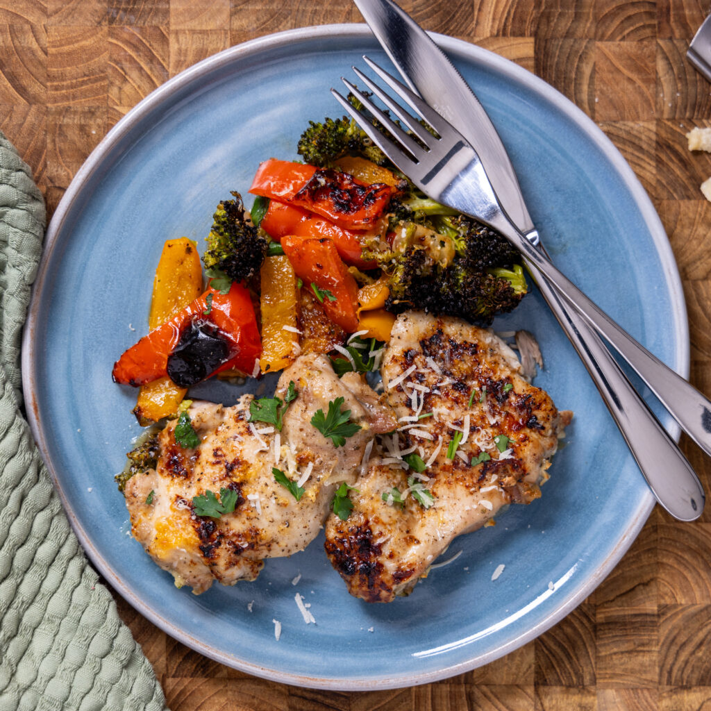 A plate with knife and fork along with a serving from a sheet pan dinner with chicken and vegetables, flavoured with balsamic vinegar and parmesan.