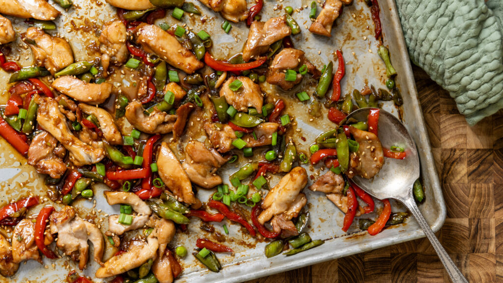 A sheet pan with chicken and vegetables, coated in a chili garlic sauce.