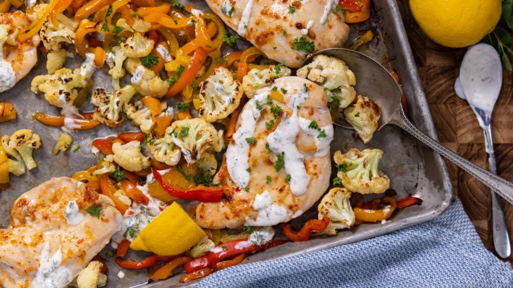 Harissa glazed chicken breast with roasted vegetables on a sheet pan.