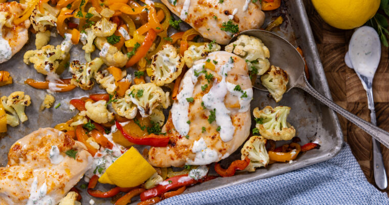 Harissa glazed chicken breast with roasted vegetables on a sheet pan.