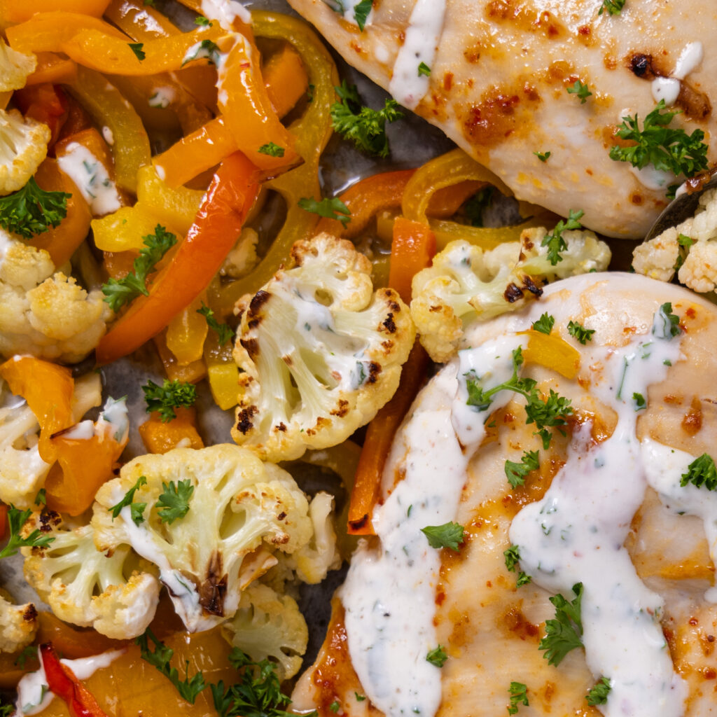 A close-up view of harissa-spiced chicken and roasted vegetables, drizzled with a herbed yogurt sauce.