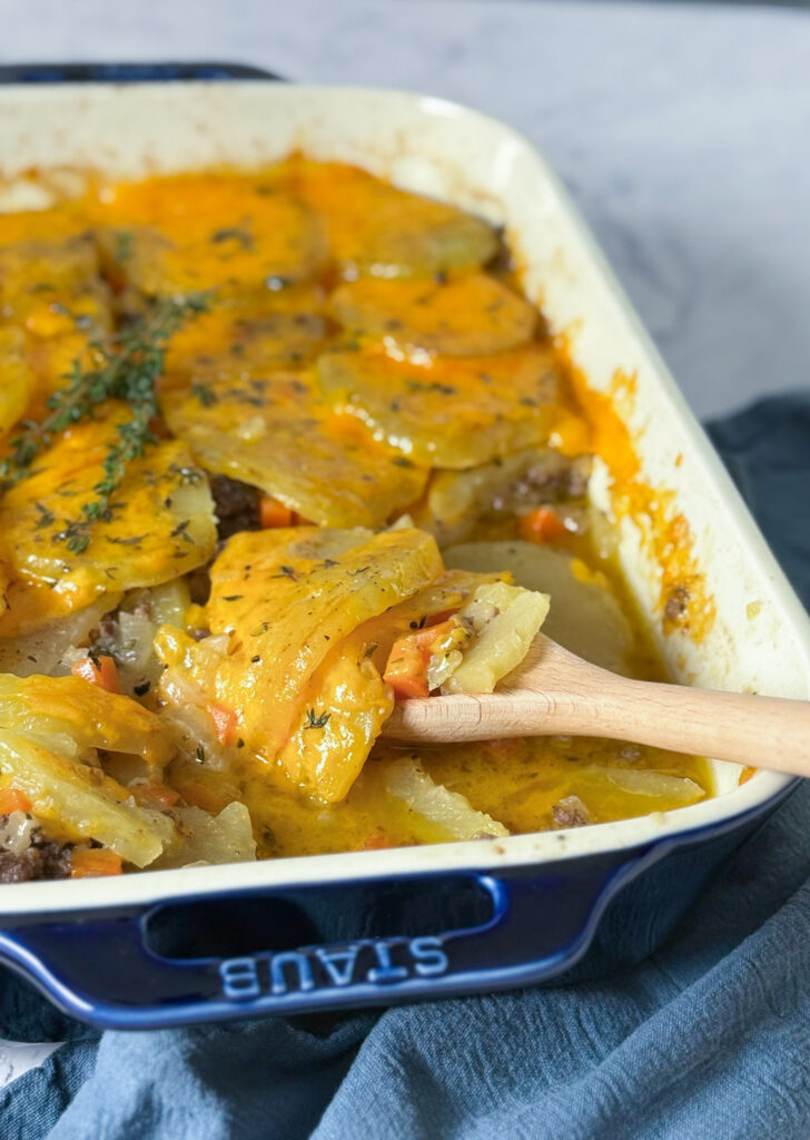 A casserole dish shows a beef and potato layered dish, covered with melted cheese.