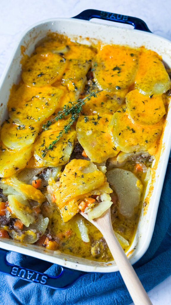 A casserole dish shows a beef and potato layered dish, covered with melted cheese.