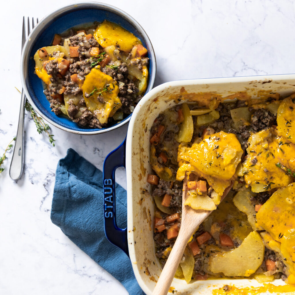 A casserole dish shows a beef and potato layered dish, covered with melted cheese.