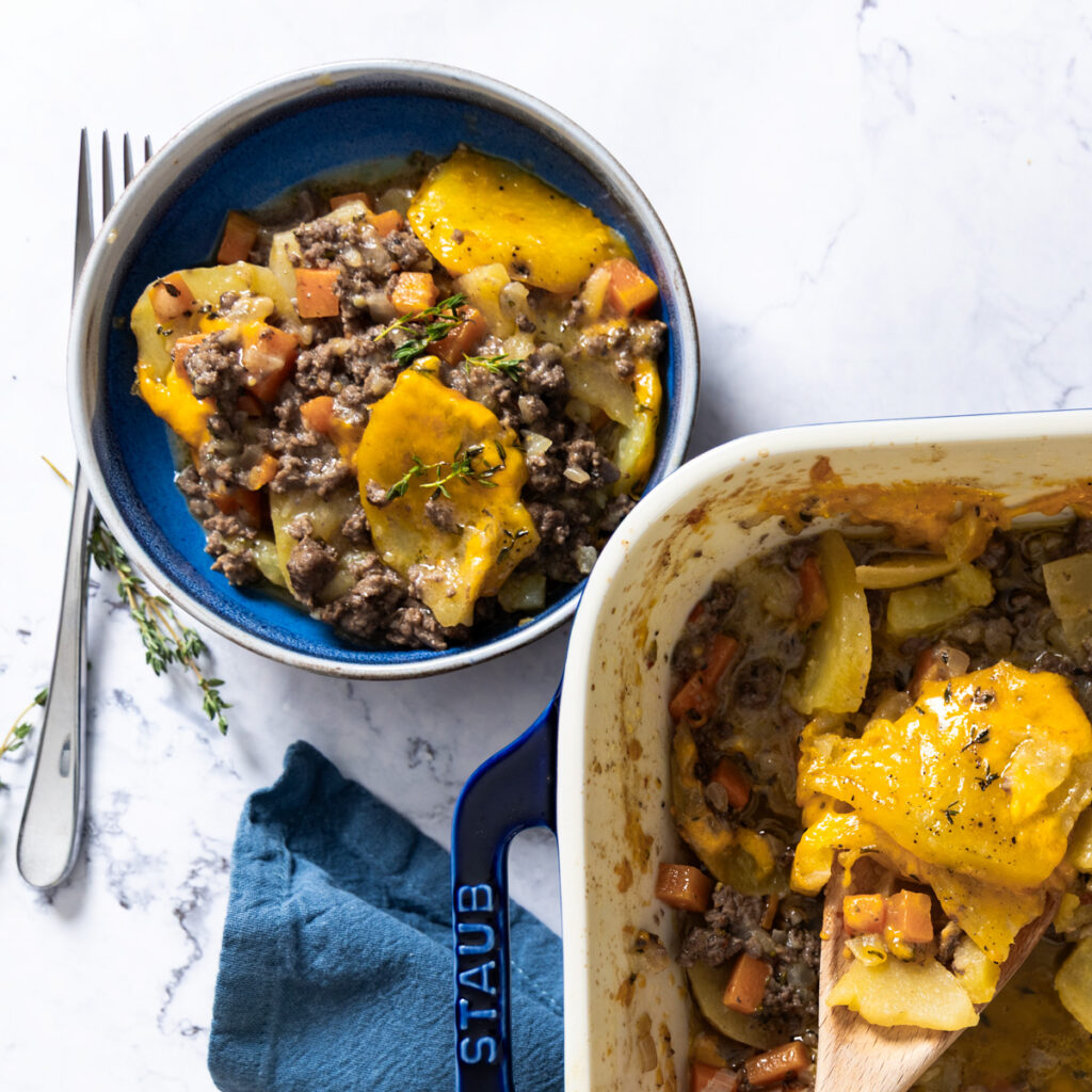 A casserole dish shows a beef and potato layered dish, covered with melted cheese.