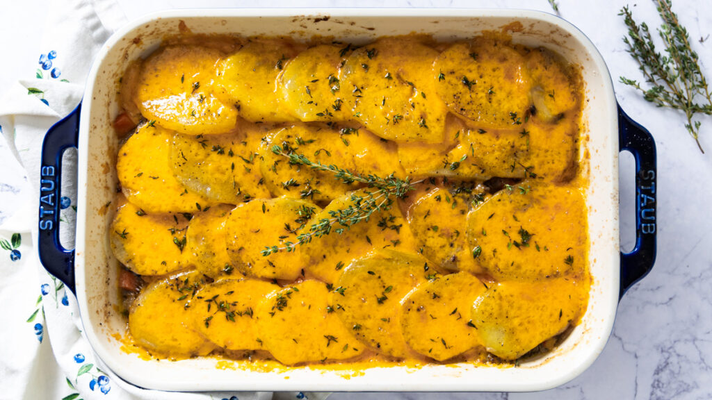 A casserole dish shows a beef and potato layered dish, covered with melted cheese.