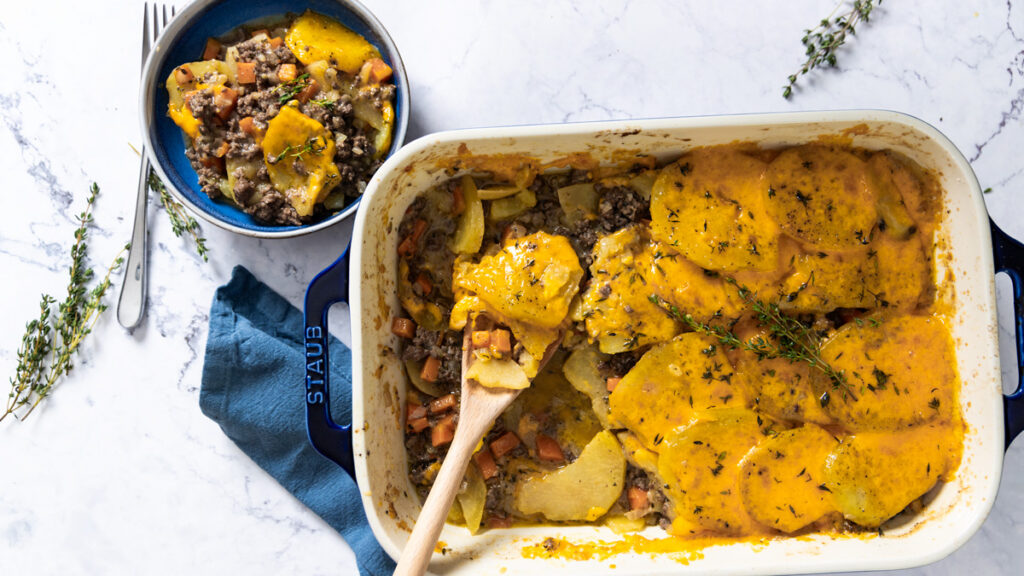 A casserole dish shows a beef and potato layered dish, covered with melted cheese.